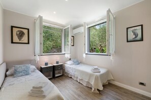 A bedroom with two beds, a nightstand, a window with curtains, and artwork on the walls. - Villa 'Due Ulivi' with Private Terrace, Private Garden and Wi-Fi (Lavagna)