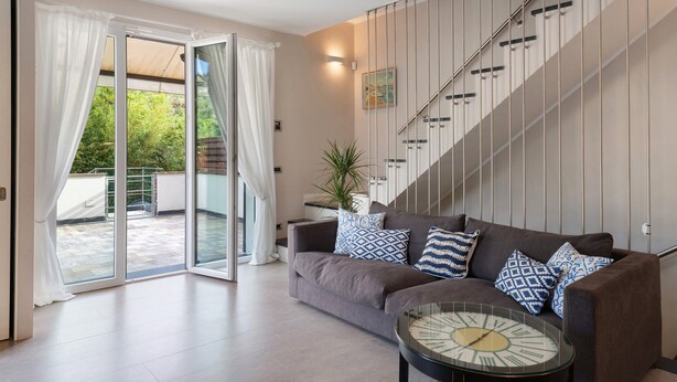 A modern living room with a sofa, patterned cushions, a glass coffee table, and a staircase. - Terraced House 'Due Ulivi' with Private Terrace, Garden, and Wi-Fi (Lavagna)