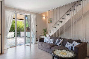 Un salon moderne avec un canapé, des coussins à motifs, une table basse en verre et un escalier.