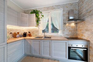 A kitchen with white cabinetry, a built-in oven, a stainless steel range hood, a window with curtains, and a plant on the counter. - Villa 'Due Ulivi' with Private Terrace, Private Garden and Wi-Fi (Lavagna)