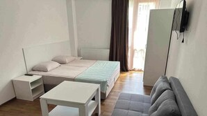 Een ruime, goed verlichte kamer met een bed, een slaapbank, een tafel en een televisie aan de muur.
