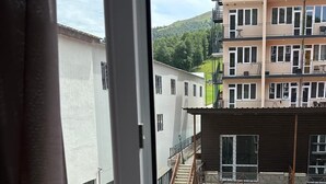 Uitzicht door een raam op een meerlaagsgebouw met balkons, een trap en een heuvel op de achtergrond.