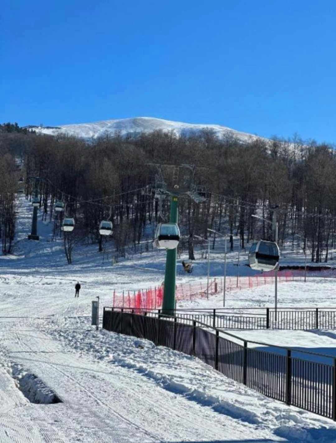 A ski lift area with a chairlift, a fenced area, and a snow-covered mountain in the background.