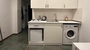 Een compacte keuken met witte kastjes, een ingebouwde wasmachine en een kleine koelkast.