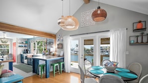 Una cocina moderna con una isla grande, taburetes de bar verdes y un comedor con mesa dispuesta para cuatro.