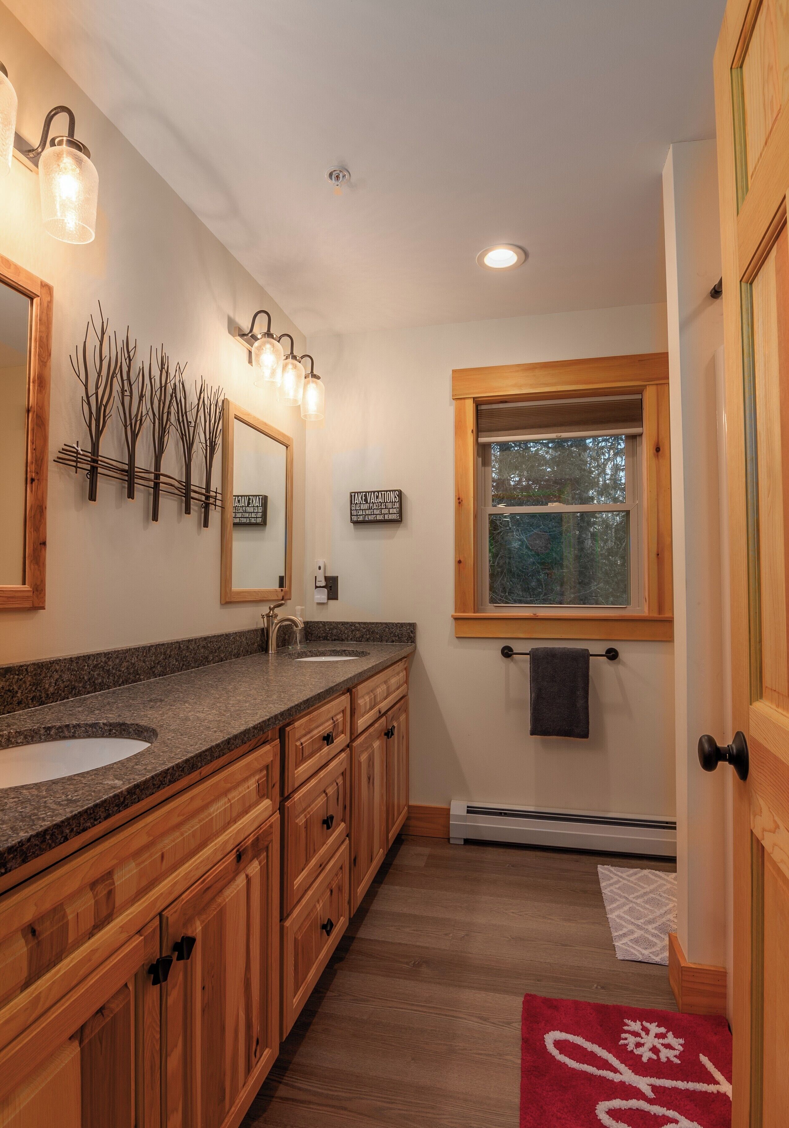 A bathroom with wooden cabinets, granite countertops, a large mirror, and a window with a view of trees.