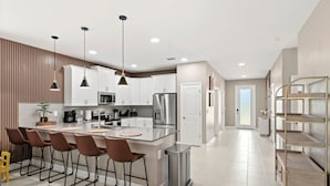 Une cuisine moderne avec des meubles blancs, des appareils en acier inoxydable et un îlot central doté de tabourets de bar.