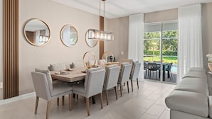 Un espace de salle à manger moderne avec une grande table, plusieurs chaises et un lustre. Trois miroirs ronds sont accrochés au mur, et une grande fenêtre offre une vue sur la verdure à l’extérieur.