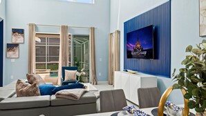 A modern living room with a large TV, comfortable seating, and a view of the outdoors. - Ultimate Disney House | Pool+Hot Tub | Game Room (Davenport)