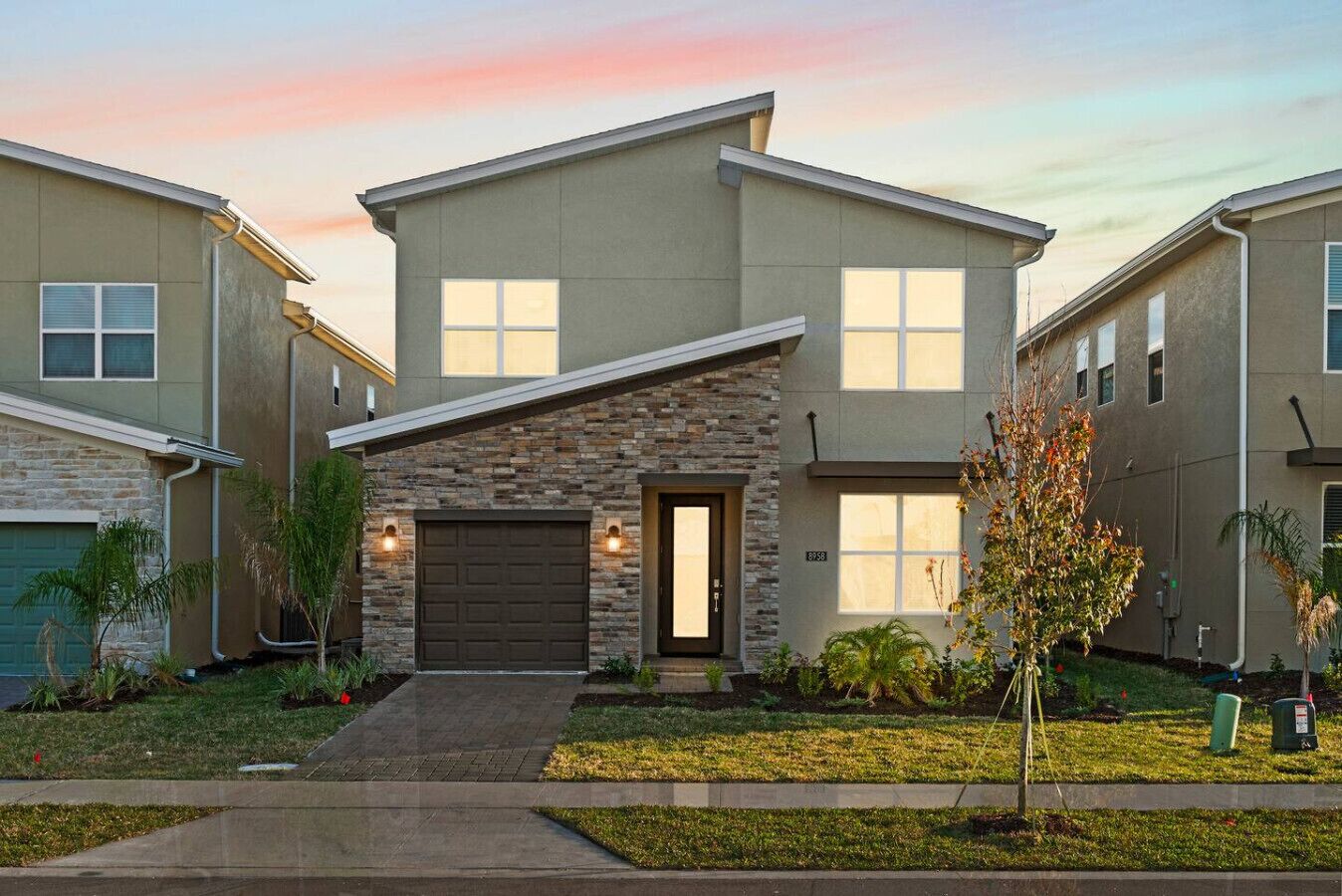 A modern two-story residential building with a stone facade, a garage, and a well-maintained front yard with landscaping.