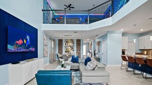 A spacious living room with a large flat-screen TV, a sofa set, and a dining area with bar stools. - Ultimate Disney House | Pool+Hot Tub | Game Room (Davenport)