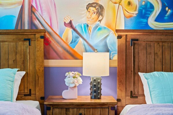 Una habitación de hotel con cabecera de madera, cama con ropa de cama blanca y azul claro, mesita de noche con lámpara y un jarrón de flores, y un mural en la pared.