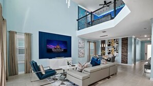 A spacious living room with a large TV, a sofa, and a dining area in the background. - Ultimate Disney House | Pool+Hot Tub | Game Room (Davenport)