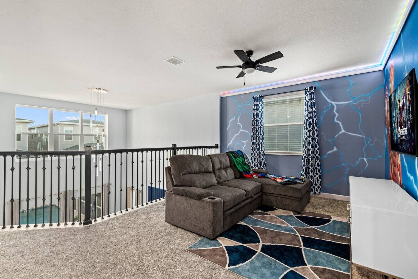 A living room with a sectional sofa, a ceiling fan, a patterned rug, and a balcony with a railing.