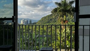 A balcony with a view of a lush green hillside and a cityscape in the distance. - Apartment in Guarujá-Enseada, leave your car in the garage, just 5 minutes from the beach (Loteamento Joao Batista Juliao Guarujá)