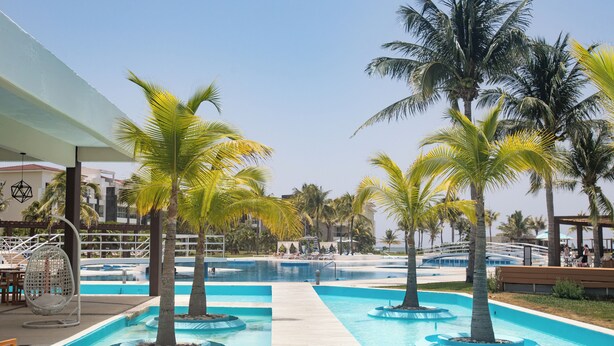 Un área de piscina con palmeras, sillones de descanso y un cielo despejado.