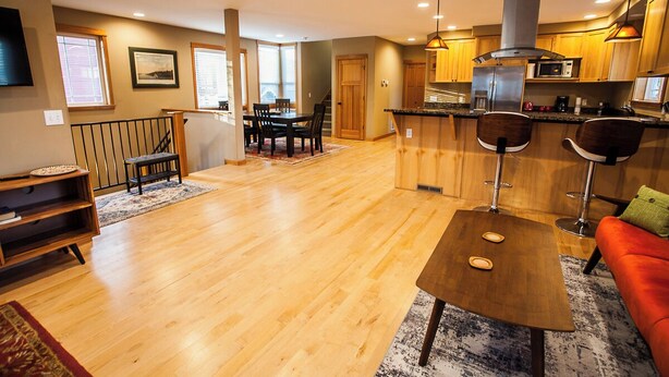 Un espacio habitable amplio con piso de madera, una mesa de comedor con sillas, una cocina con armarios de madera y un sofá rojo.