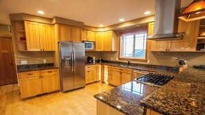 Cocina moderna con gabinetes de madera, encimeras de granito y electrodomésticos de acero inoxidable, además de un ventanal que proporciona luz natural.