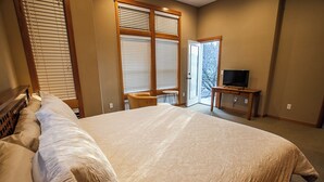 Un dormitorio con una cama grande, un televisor sobre un soporte de madera y un ventanal corredizo que da a un balcón.