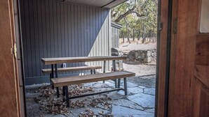 A wooden bench outside a building with a stone floor and scattered leaves.
