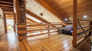 A wooden interior with a loft bed, a stone wall, and a wooden staircase.