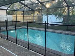 A covered swimming pool with a metal fence, surrounded by a wooden fence and trees. - Retreat off Main Street (Safety Harbor)