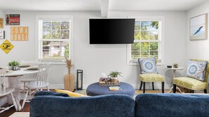A living room with a white dining table, two blue sofas, a TV, and a window with blinds. - Retreat off Main Street (Safety Harbor)