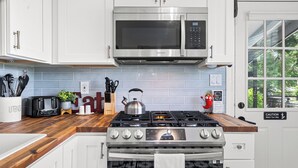 A kitchen with white cabinets, a stainless steel microwave, a gas stove, and a tiled backsplash. - Retreat off Main Street (Safety Harbor)