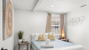 A bedroom with a bed, bedside table, lamp, and a window with curtains. - Retreat off Main Street (Safety Harbor)