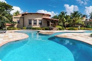 A swimming pool with a curved design, a house with a red-tiled roof, and palm trees. - Villa Esplanade- Seascape Villas (San Pedro)
