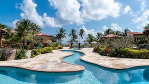A swimming pool with a curved design, surrounded by palm trees and a clear blue sky. - Villa Esplanade- Seascape Villas (San Pedro)
