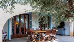An outdoor dining area with a wooden table and chairs, a grill, and a covered entrance.