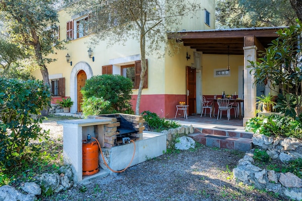 A courtyard with a stone bench, a barbecue grill, and a dining area with outdoor furniture.