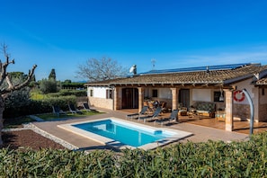 Une maison avec une piscine, un espace extérieur aménagé et un ciel d’un bleu éclatant.
