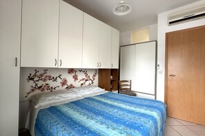 Une chambre à coucher avec un lit, des armoires blanches, une porte en bois et une fenêtre ornée de motifs floraux.