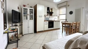 A compact kitchen with a dining area, a TV on a stand, and a bed in the foreground. - SE131 - Senigallia, two-room apartment with air conditioning and terrace (Senigallia)