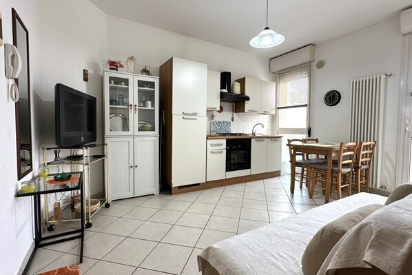 Une cuisine compacte avec un coin repas, un téléviseur posé sur un meuble et un lit en premier plan.