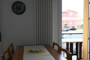 Un espace repas comprenant une table, des chaises, une horloge et une fenêtre donnant sur des immeubles et des voitures.