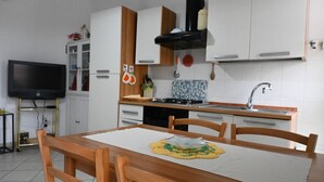 A compact kitchen with white cabinets, a black range hood, a tiled backsplash, and a dining table with chairs. - SE131 - Senigallia, two-room apartment with air conditioning and terrace (Senigallia)
