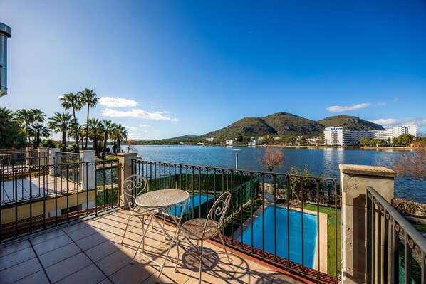 A terrace with a pool, palm trees, and a view of a lake and mountains.