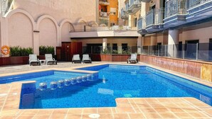 Ein Schwimmbecken mit Fliesenstufen, umgeben von Liegestühlen und einer Holzterrasse.