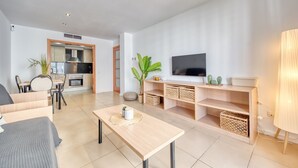 Ein modernes Wohnzimmer mit Sofa, Couchtisch, Fernseher und einer Küche im Hintergrund.