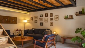 A modern living room with a staircase, wooden beams, a sofa, a coffee table, and framed pictures on the wall. - Departamento Emilio Dondé zona céntrica CDMX (Ciudad de México)