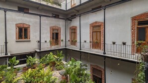 A courtyard with potted plants, a brick wall, and a balcony with railings. - Departamento Emilio Dondé zona céntrica CDMX (Ciudad de México)