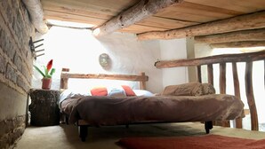 Ein rustikales Schlafzimmer mit einem hölzernen Bett, einem kleinen Nachttisch mit einer Topfpflanze und einem roten Teppich auf dem Boden.