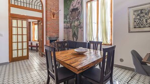 A dining area with a wooden table and chairs, a large mural on the wall, and a tiled floor. - Conjunto 3 apartamentos en Centro Historico (Santiago de Querétaro)