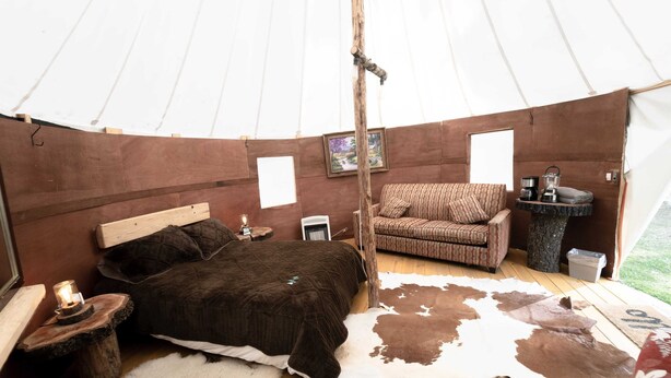 L’intérieur accueillant d’une tente, avec un lit, une chaise, une petite table avec une lampe et un tapis en peau de vache.