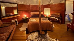 Una habitación con tienda de campaña acogedora, una cama en el centro, suelo de madera, un espejo y un farol rústico.