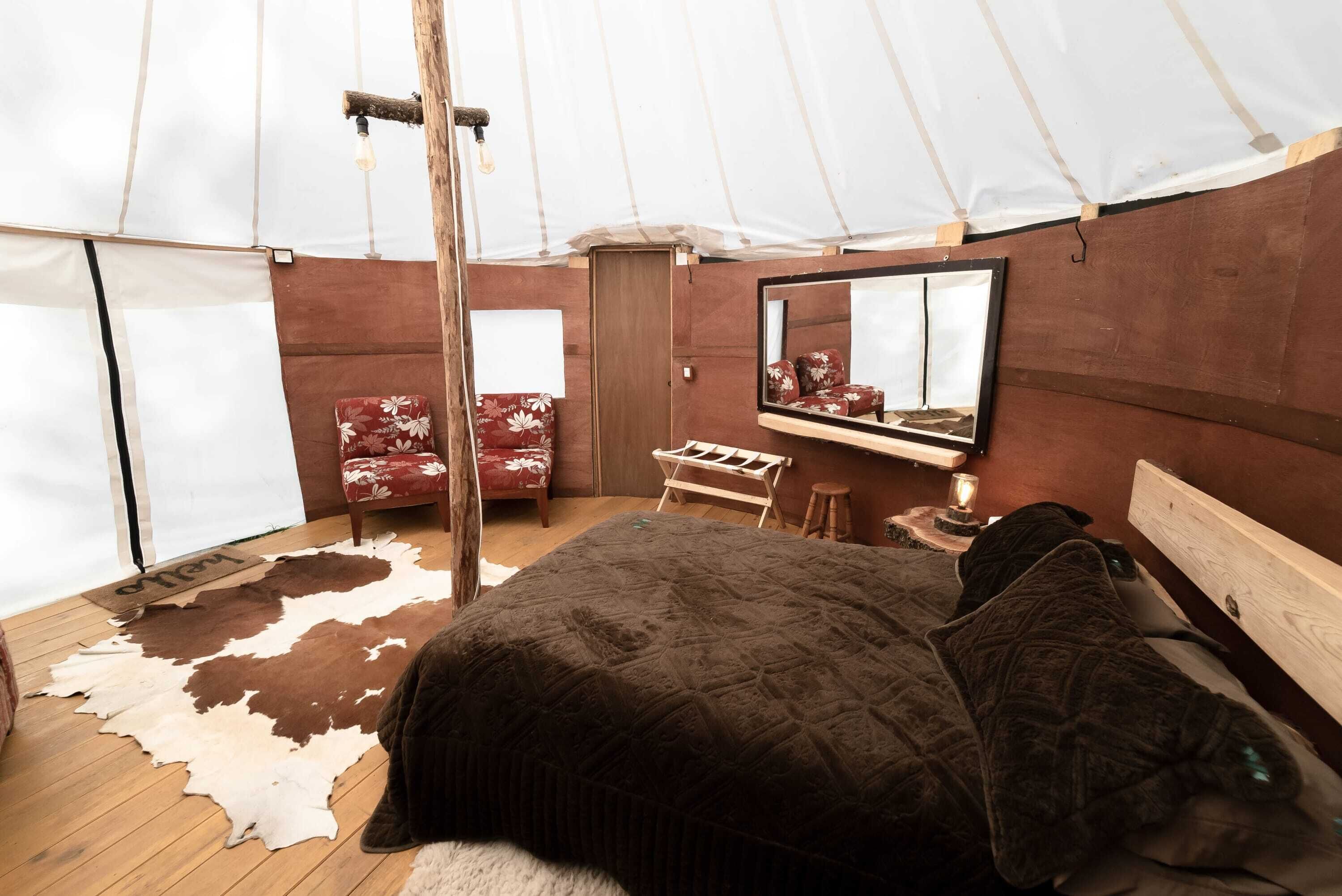 A tent-style room with a bed, a chair, a mirror, and a wooden bench.