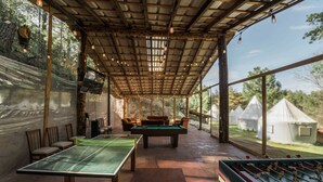 Un espace de loisirs intérieur comprenant une table de ping-pong, un baby-foot et un coin salon situé sous un toit en bois doté de grandes fenêtres.